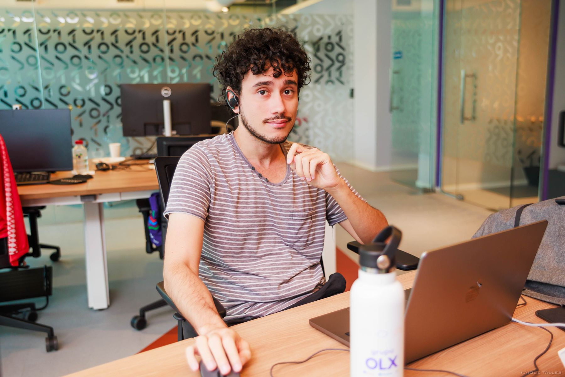 Homem de cabelo cacheado sorrindo ao lado de um notebook